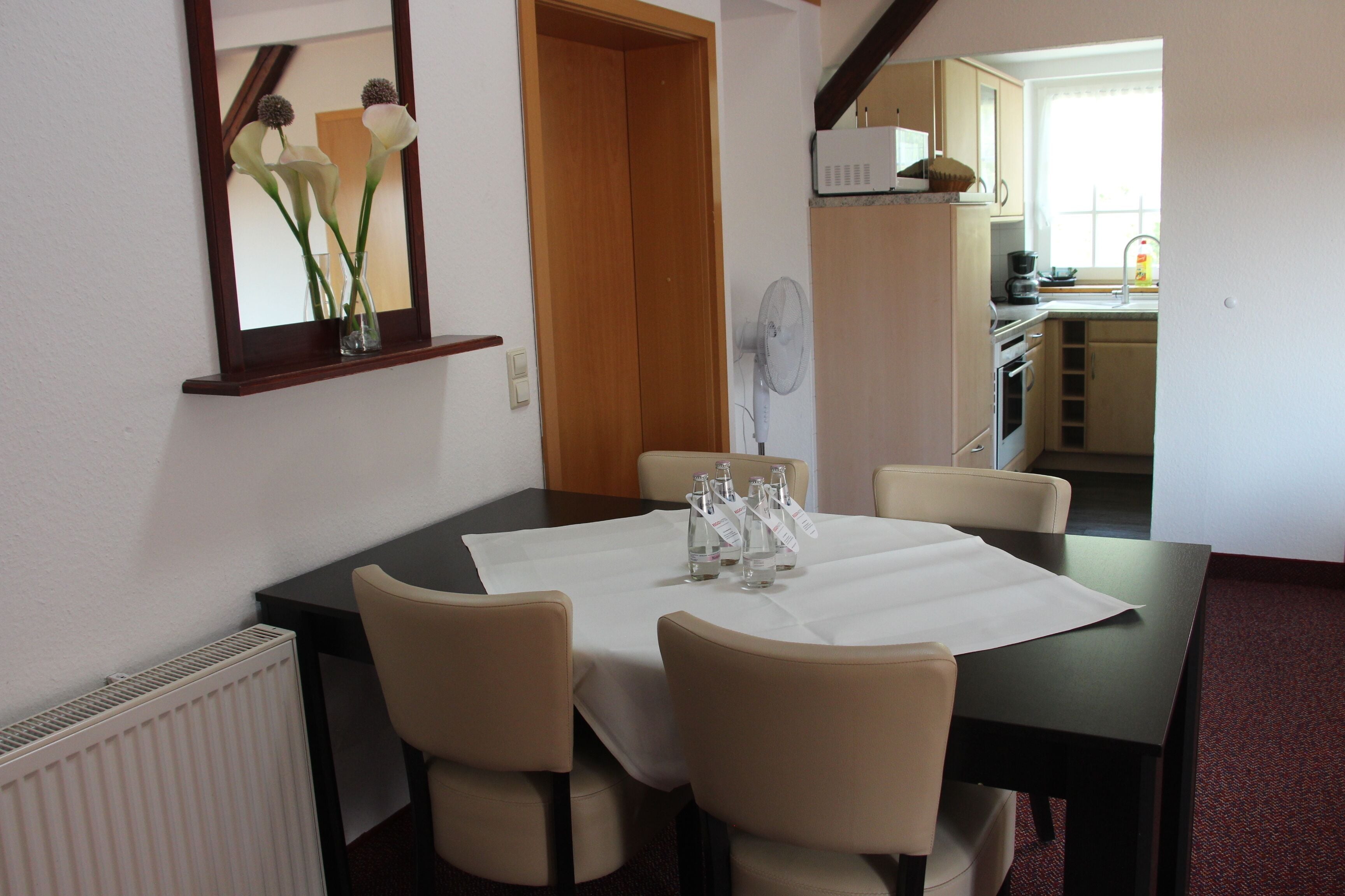 A dining area with a table set for four, a mirror, and a view into the kitchen.