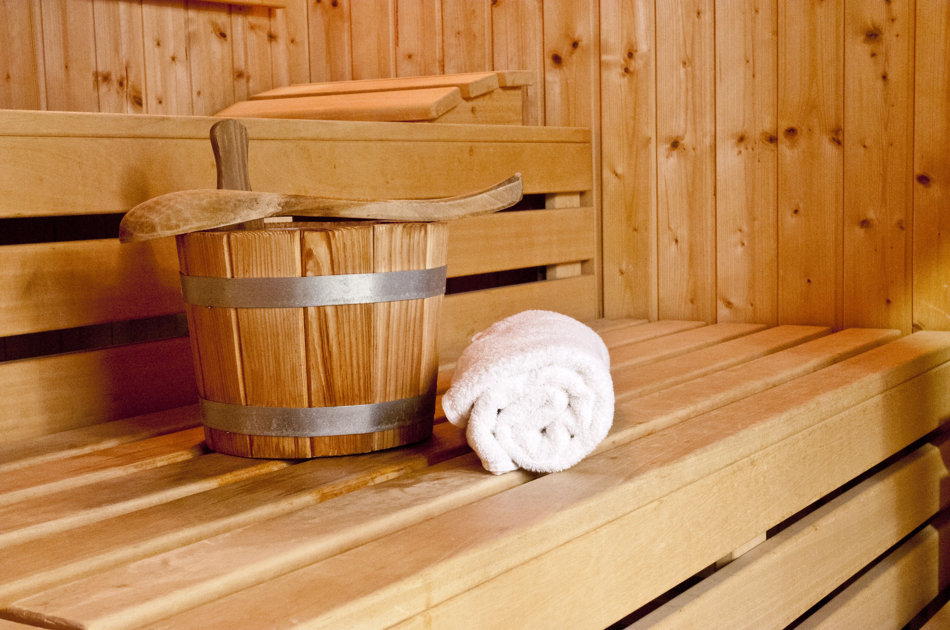 A wooden bench with a wooden bucket and a rolled-up towel.
