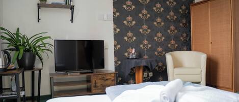 A hotel room with a bed, a television, a chair, a small table with a plant, and a wardrobe.