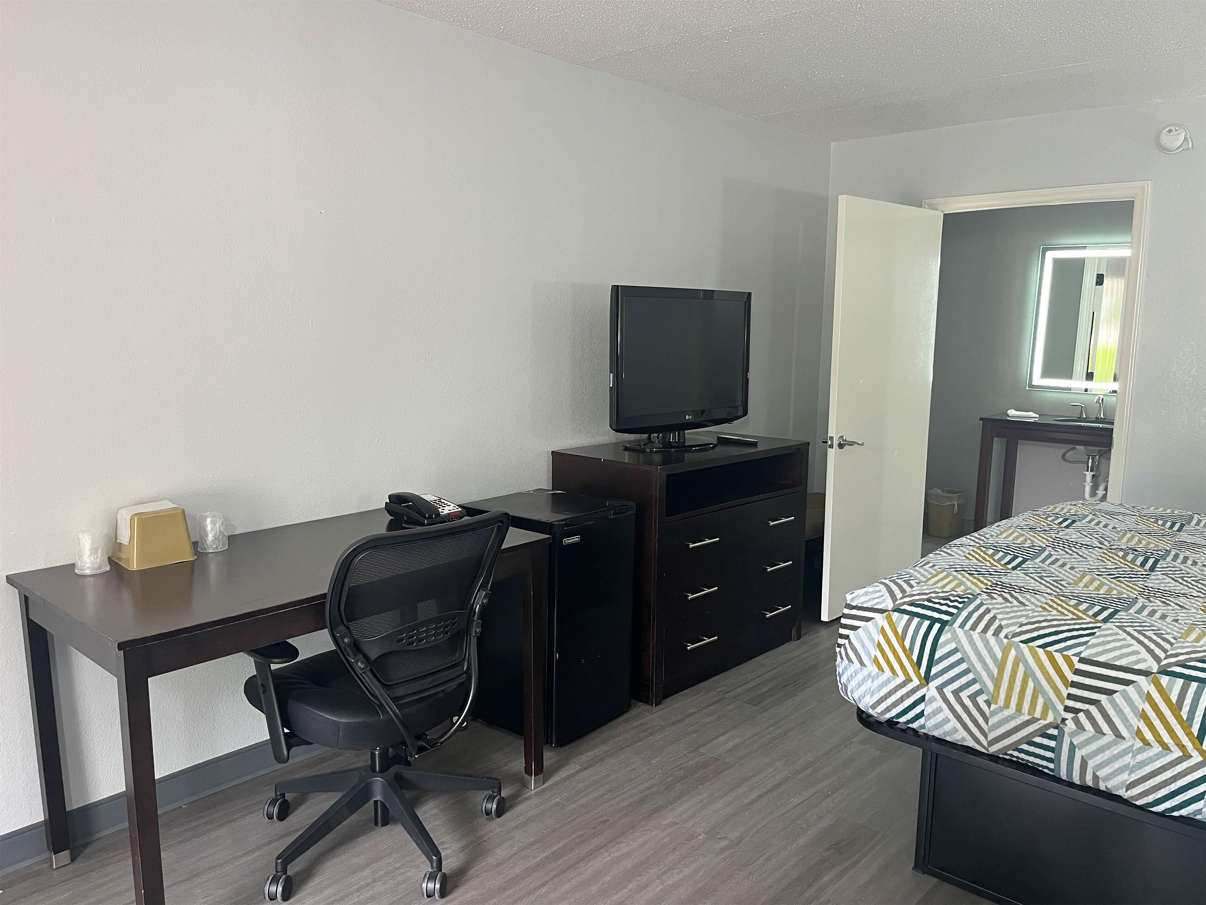 A compact hotel room with a bed, a desk with a computer, a chair, a TV, and a dresser.