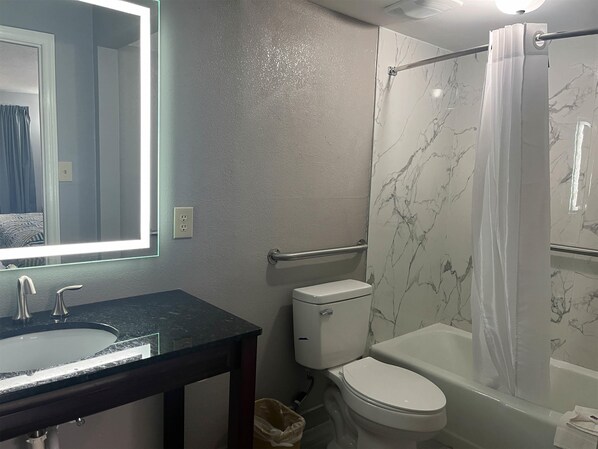 A bathroom with a marble wall, a bathtub, a toilet, and a sink with a mirror.