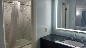 A bathroom with a marble shower wall, a white toilet, and a dark vanity with a large mirror. - Motel 6 – Spindale, NC – Forest City (Spindale)