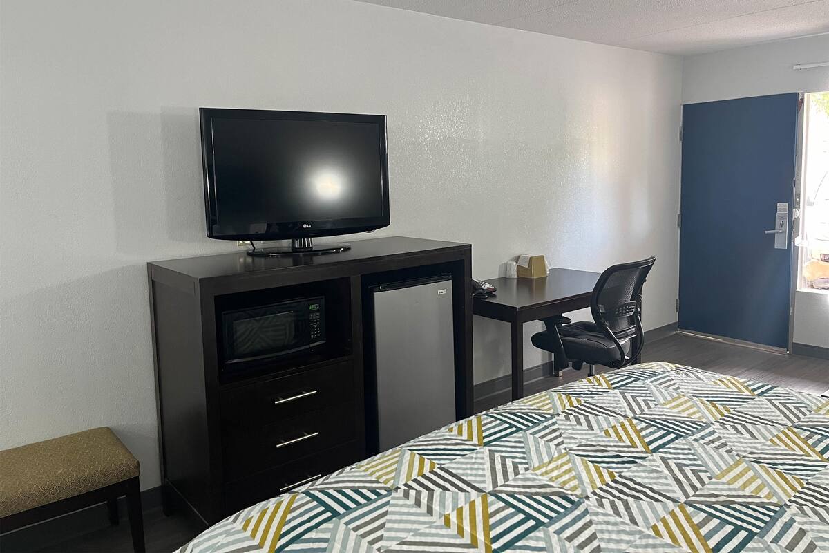 A hotel room with a bed, a desk with a television, a microwave, and a chair.