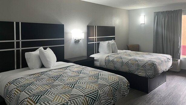 A hotel room with two beds, a nightstand, a wall-mounted lamp, and a window with curtains. - Motel 6 – Spindale, NC – Forest City (Spindale)