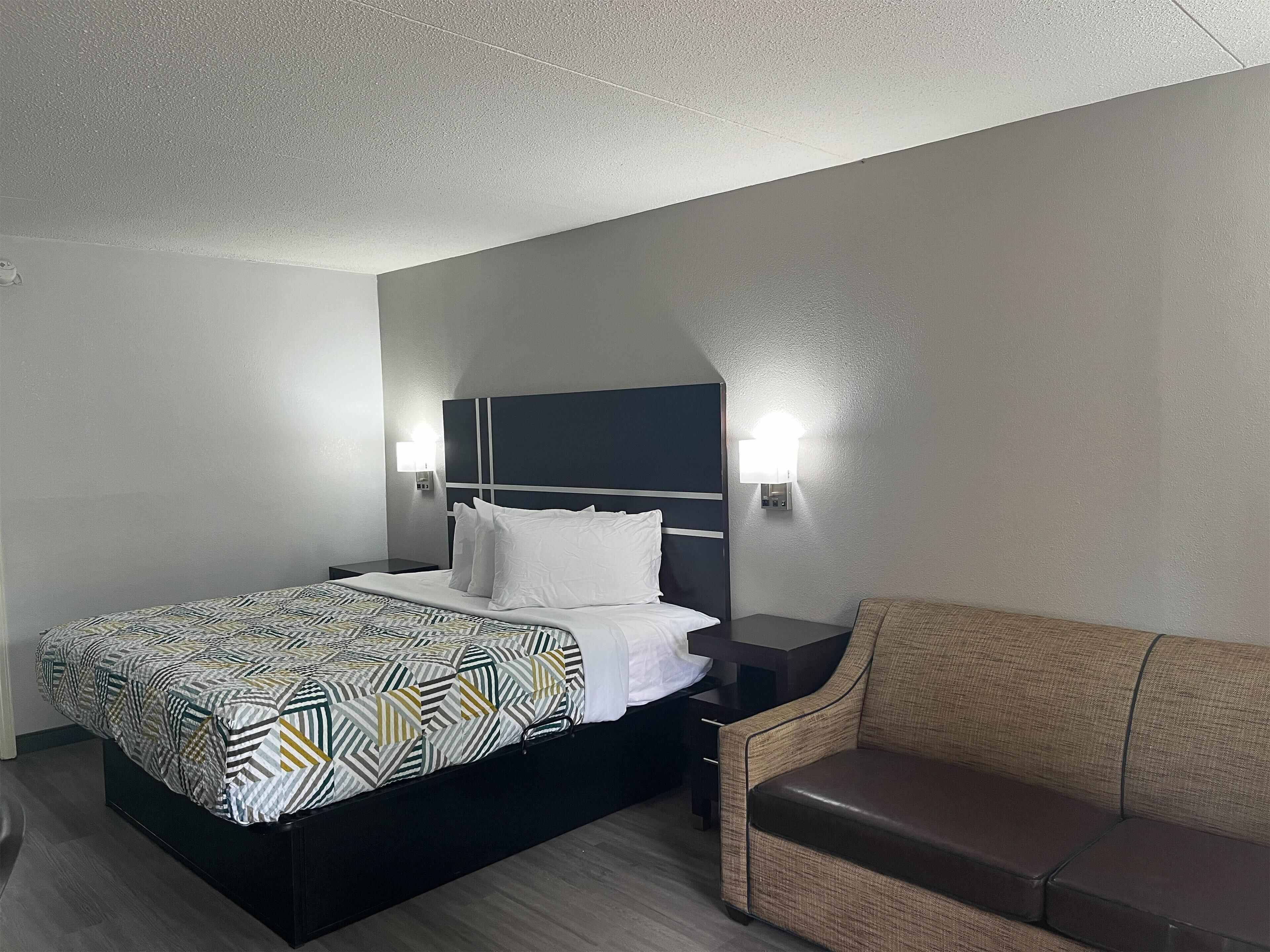 Una habitación de hotel con cama, mesitas de noche, un sofá e iluminación en la pared.