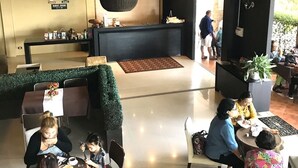 Un hall de hotel con mostrador de recepción, zona de estar y un seto verde.