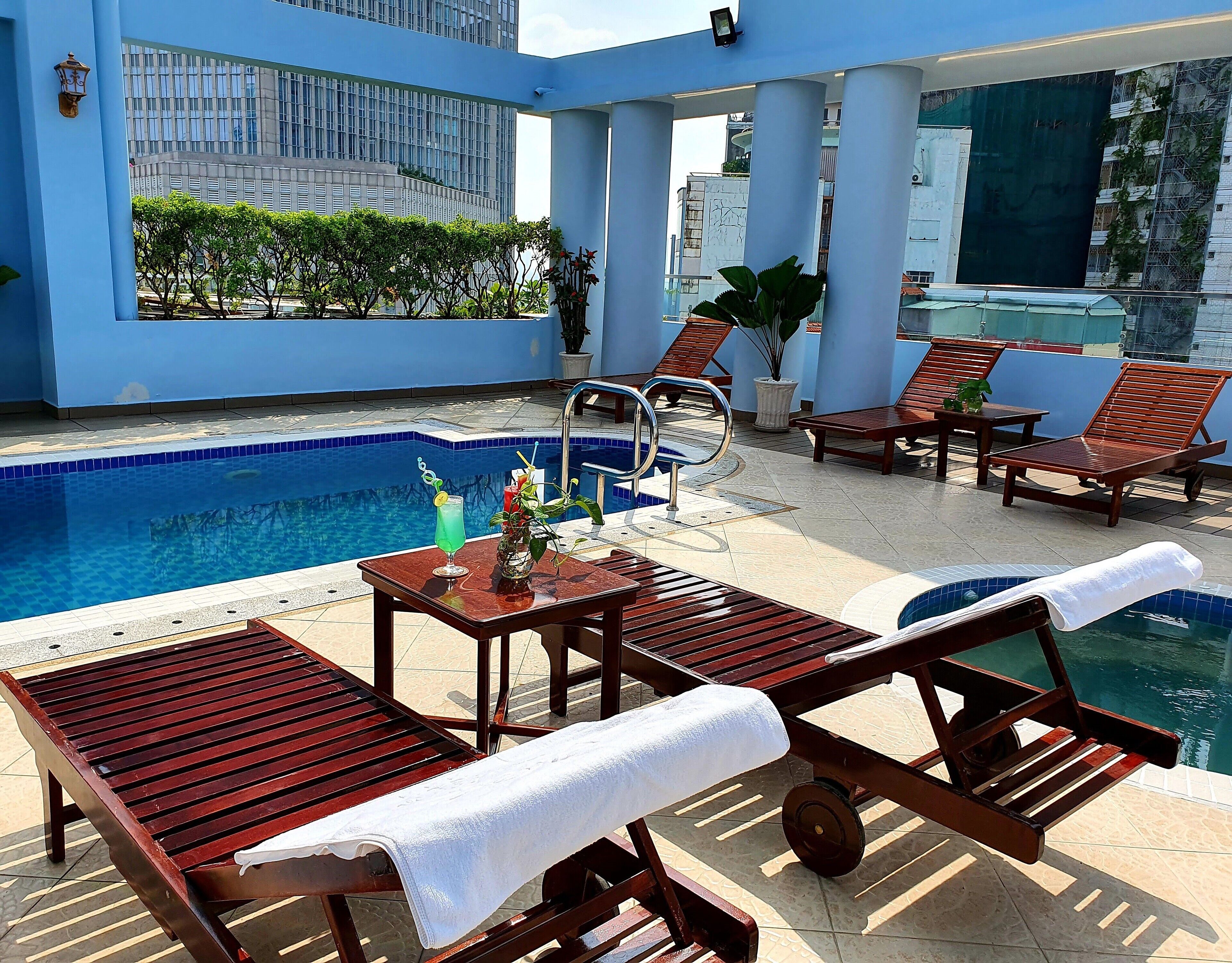 Un área de piscina en la azotea con sillones de descanso, una mesa con bebidas y vistas a un edificio moderno.