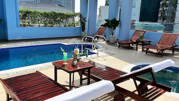 Un área de piscina en la azotea con sillones de descanso, una mesa con bebidas y vistas a un edificio moderno.
