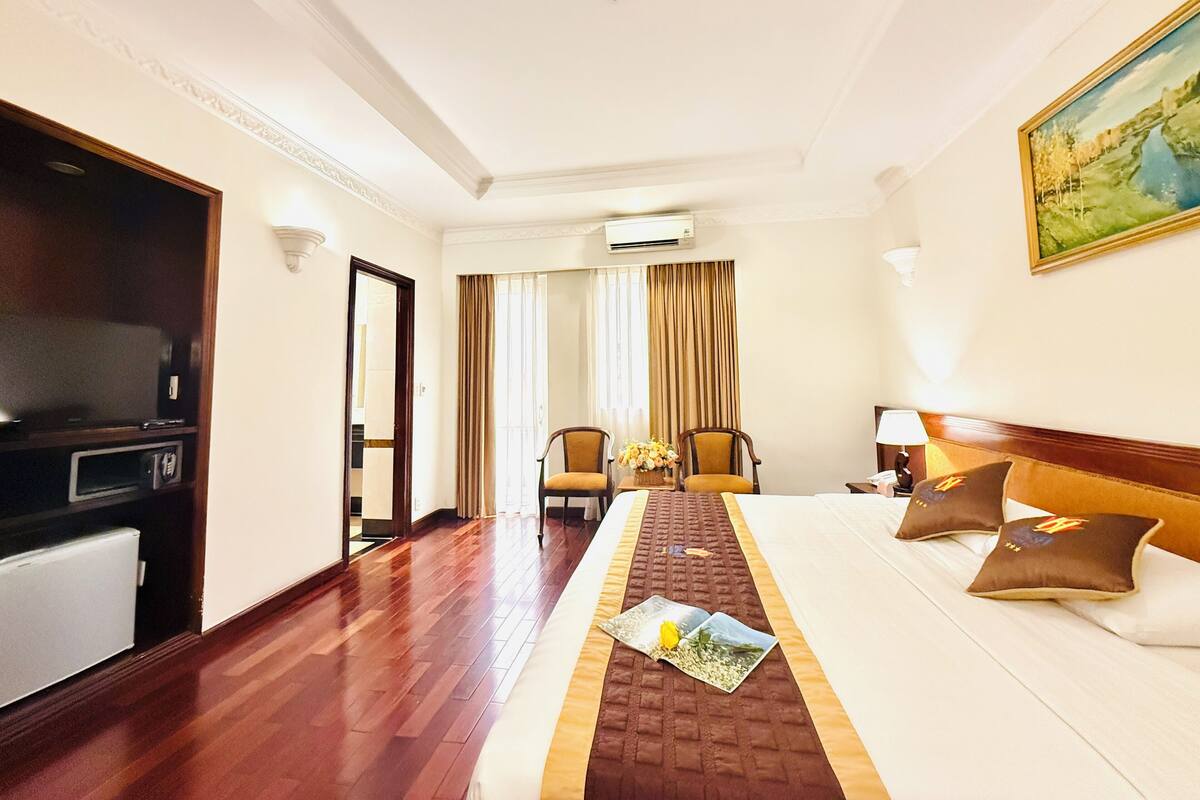 Una habitación de hotel con cama, televisión, escritorio y ventana con cortinas.