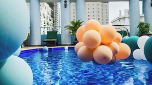 Una piscina en la azotea con suelo de mosaicos azules, rodeada de grandes esferas decorativas y una estructura arquitectónica moderna.