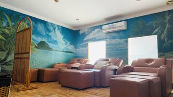 A room with a massage chair, a wooden floor, and a mural of a tropical beach.