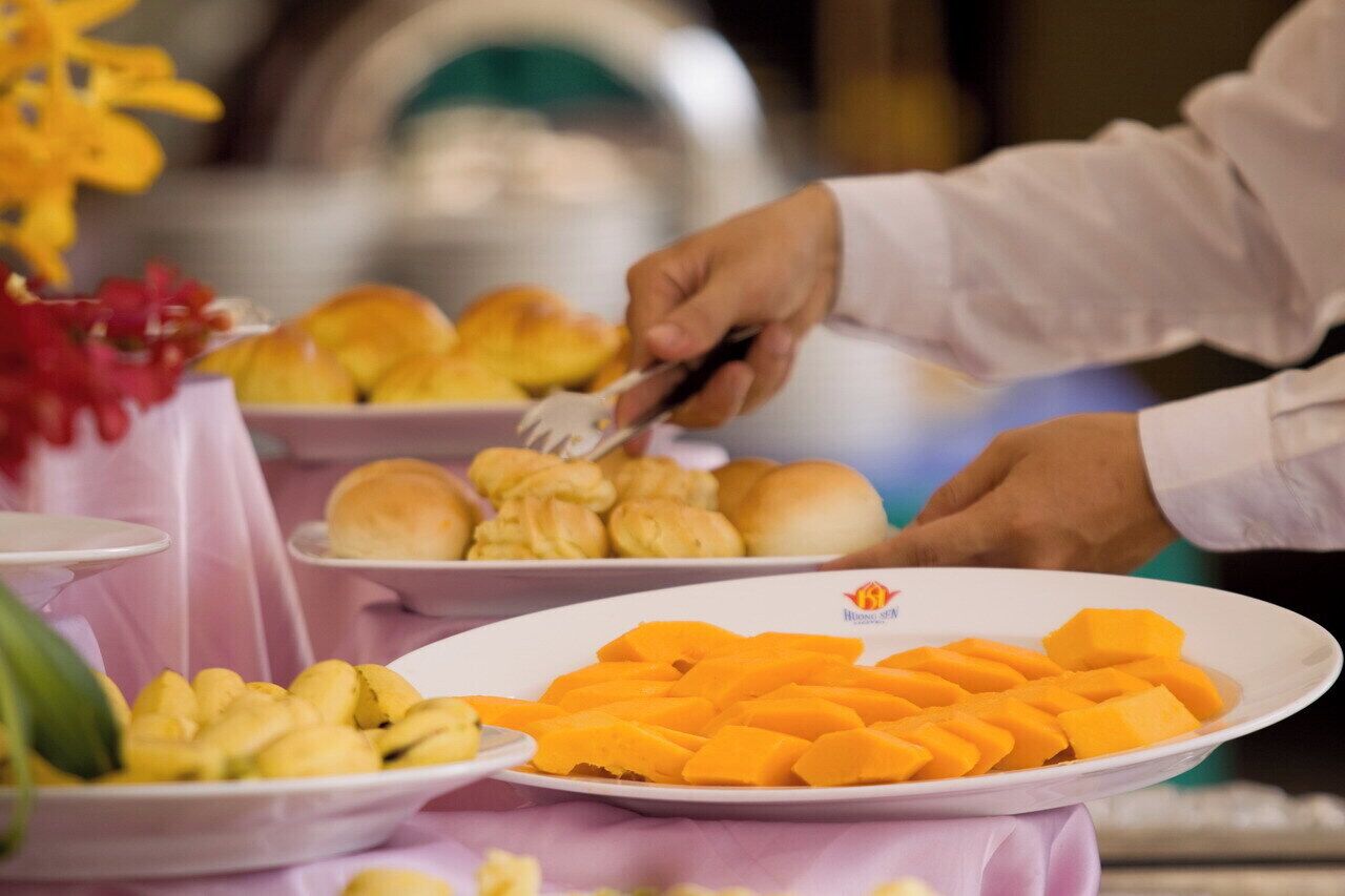 Un bufé con diversos alimentos, incluyendo panes, fruta, y un plato con un logotipo.