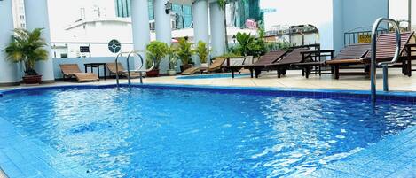 Una piscina con sillas de descanso y plantas en macetas, rodeada de edificios modernos.