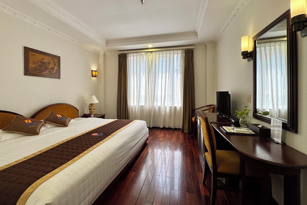 Una habitación de hotel con una cama grande, un escritorio con una silla, un televisor y una ventana con cortinas.