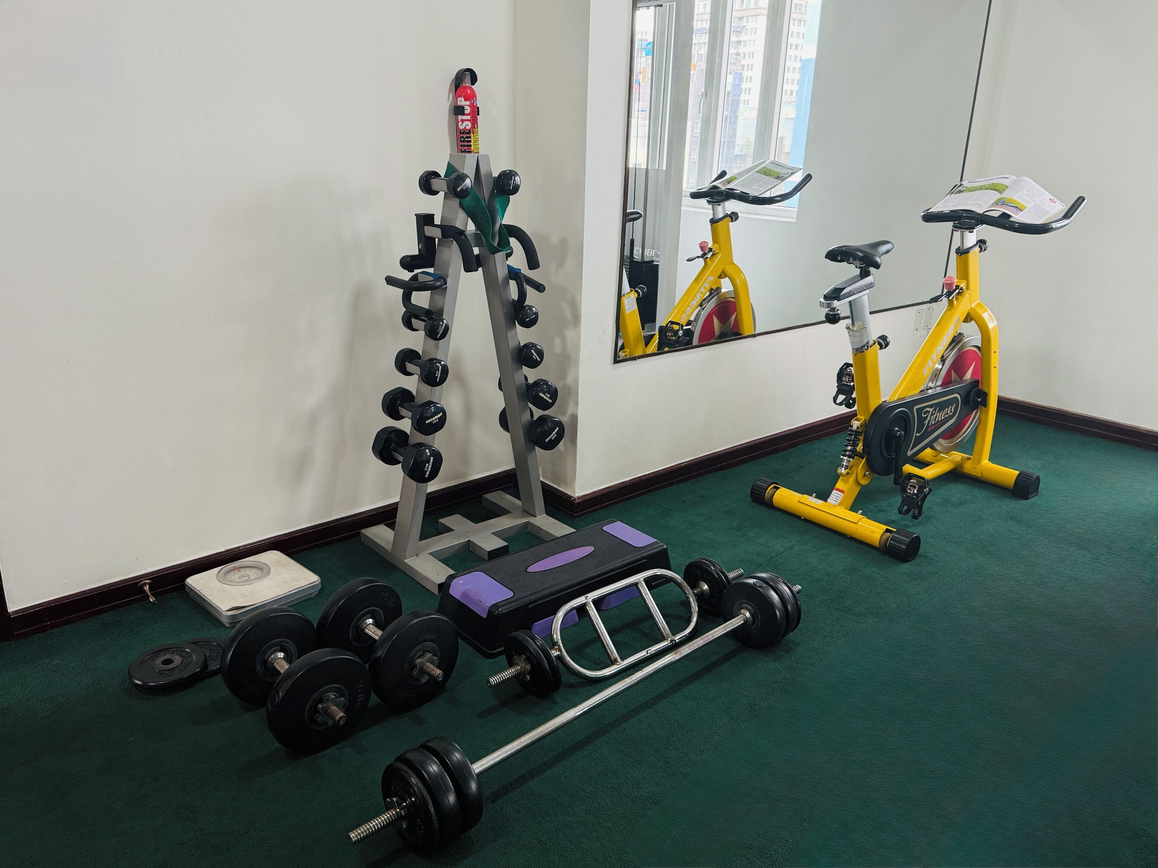 Een sportschool met een gewichtrek, dumbbells, een halter en een hometrainer.