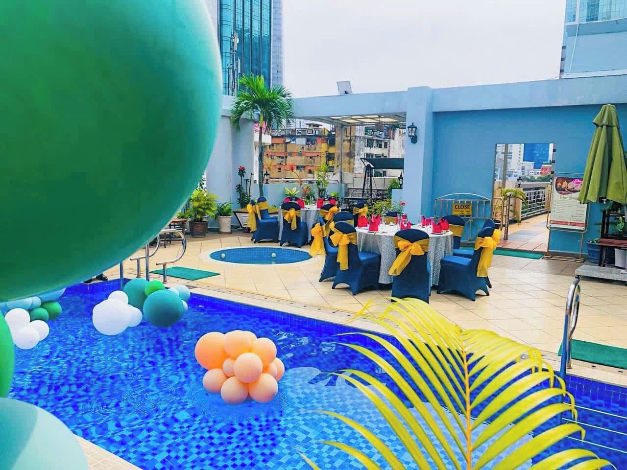 A rooftop pool area with blue water, yellow and blue chairs, and tables set up for dining.