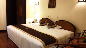 A hotel room with a large bed, a bedside table with a lamp, a chair, and a small table with a plant.