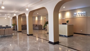 A modern hotel lobby with a reception desk, seating area, and a large sign reading "The Phoenix Bangkok".