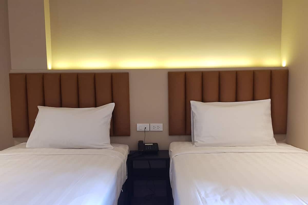 A hotel room with two beds, each with white linens and pillows, a brown headboard, and a bedside table with a phone and charger.