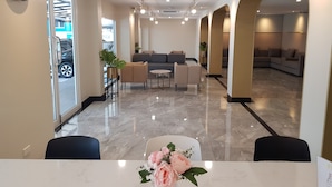 A hotel lobby with a marble floor, seating area with sofas and chairs, a clock on the wall, and a reception desk with a vase of flowers.