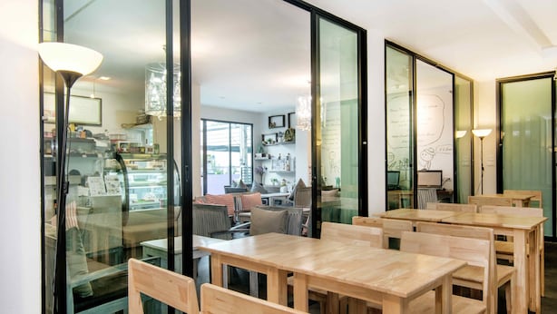 A modern interior with wooden tables and chairs, large windows, and a visible kitchen area.