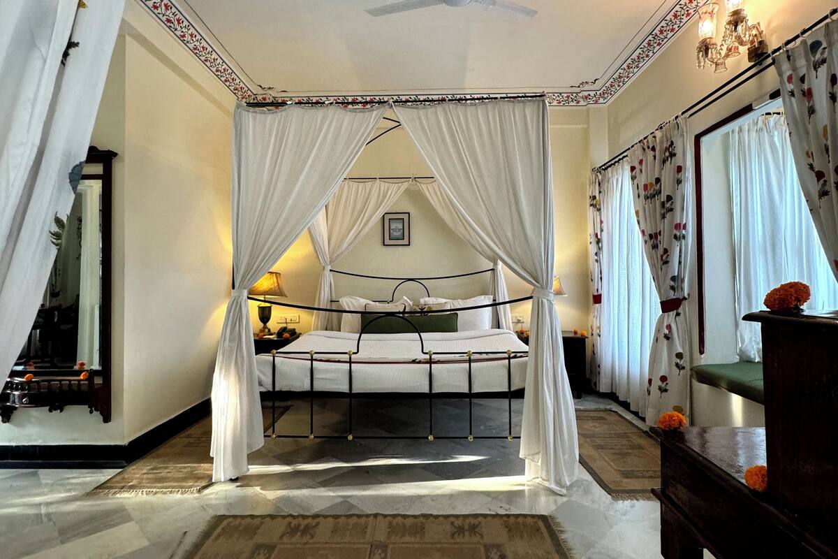 A bedroom with a four-poster canopy bed, a ceiling fan, and a large mirror.