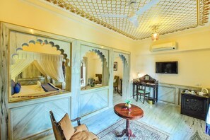 Cozy retreat with a bed, seating area, and television, set against a decorative ceiling with a net-like pattern.