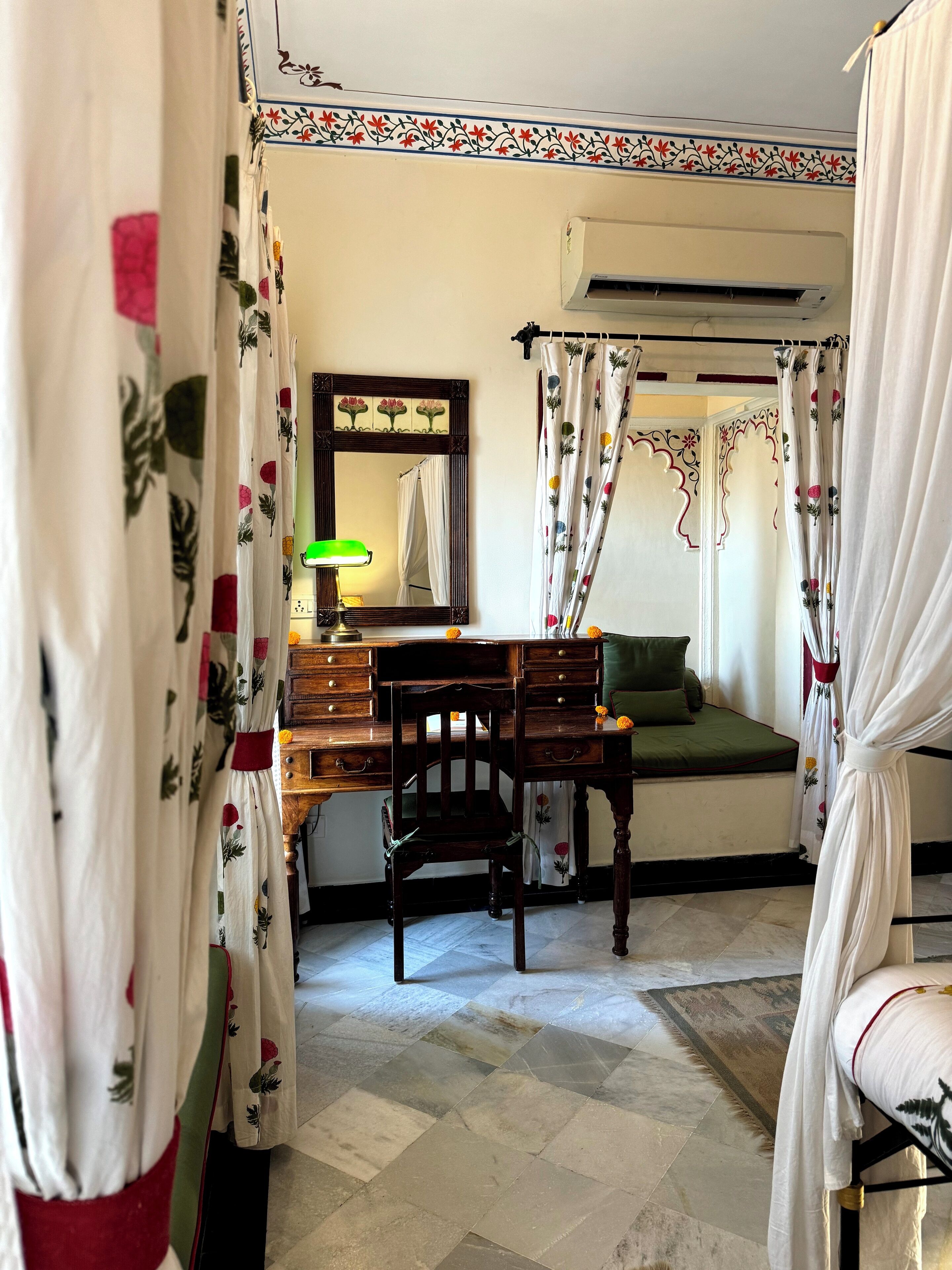 Una habitación con cama, escritorio, silla, aire acondicionado y espejo.