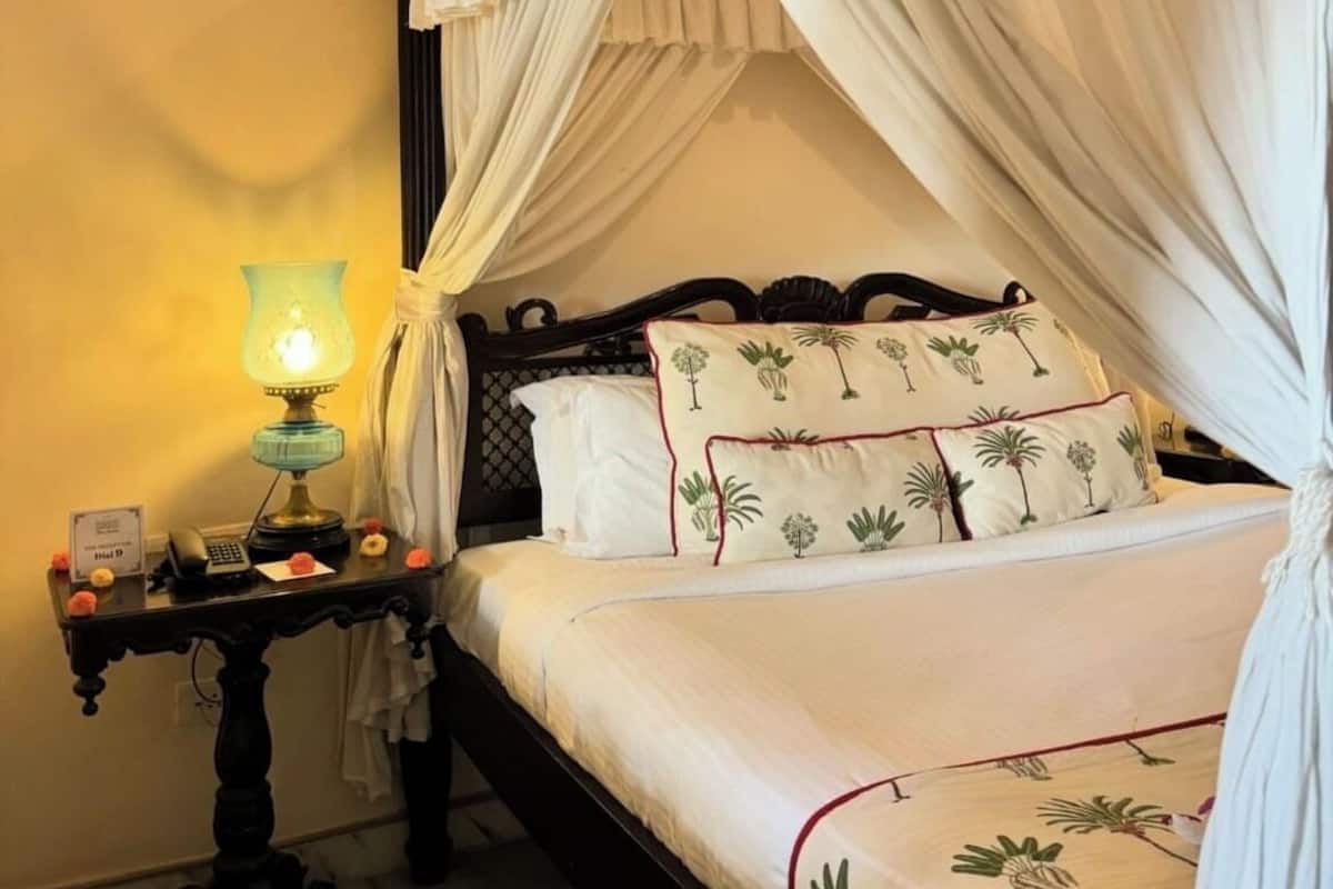 A bed with a canopy, a bedside table with a lamp, and a patterned bedspread.