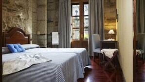 Une pièce avec un mur en pierre, un lit en bois avec une couette à carreaux, une chaise et une table avec une lampe.