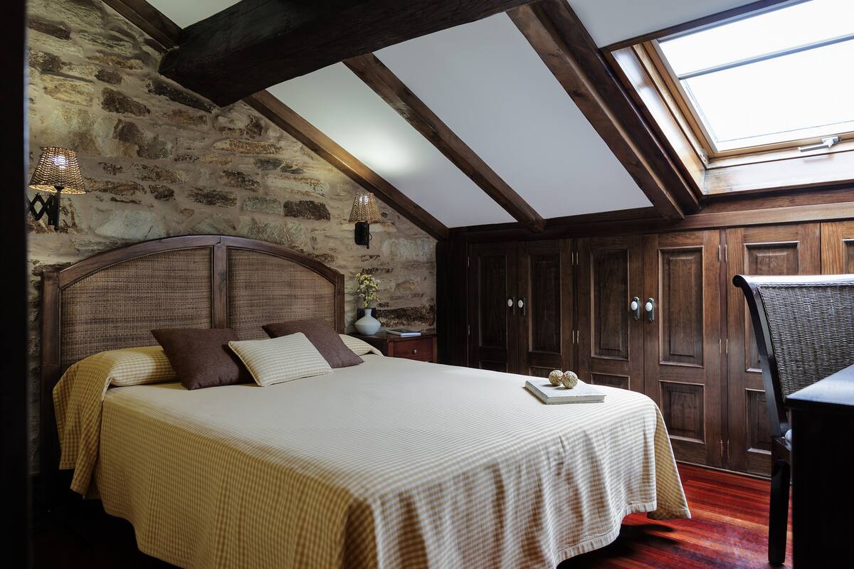 A bedroom with a large bed, wooden wardrobe, and a skylight.