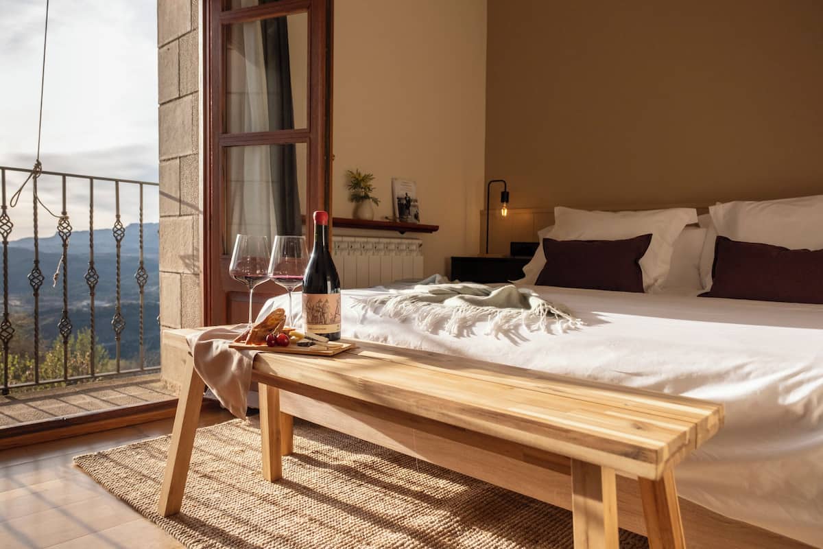 Ein Schlafzimmer mit einem großen Bett, einer hölzernen Bank, einer Weinflasche und Gläsern auf einem Tisch.