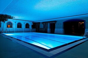 Une piscine intérieure dotée d’un plafond éclairé en bleu et de murs en pierre.