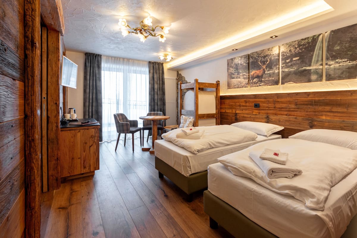 A hotel room with two beds, a wooden headboard, a desk with a chair, a small table, and a large window with a nature scene.