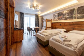 Une chambre d’hôtel avec deux lits, une tête de lit en bois, un bureau avec une chaise, une petite table et une grande fenêtre donnant sur un paysage naturel.