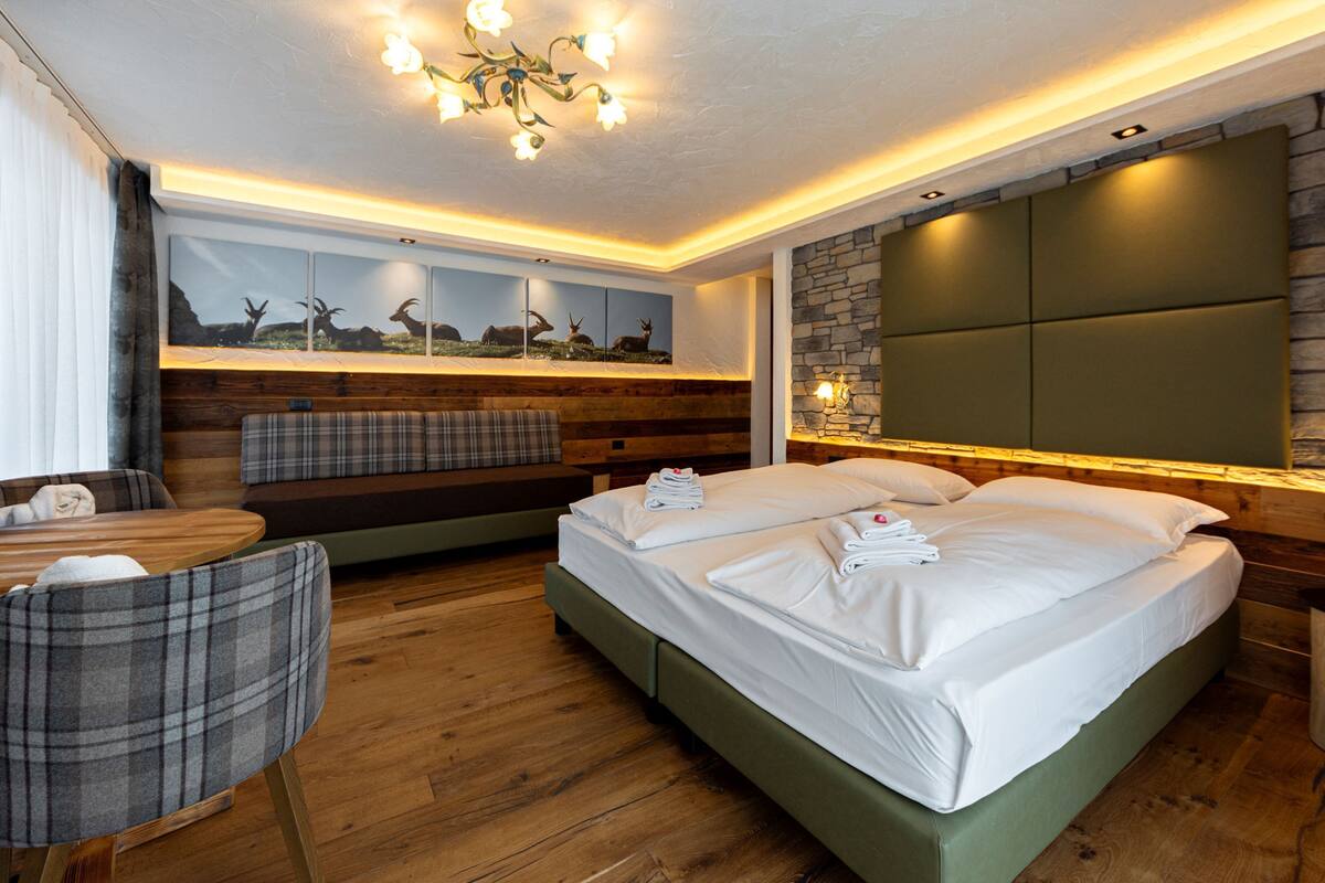 A modern hotel room with a large bed, a wooden floor, a seating area with a table and chairs, and a wall-mounted TV.