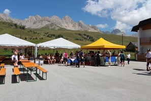 Un événement en plein air avec des tables et des tentes, une foule de personnes et des montagnes en arrière-plan.
