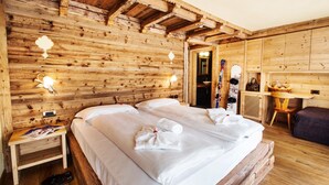 A wooden cabin room with a bed, bedside table, and skis leaning against the wall. - Hotel Arnika Wellness (Moena)