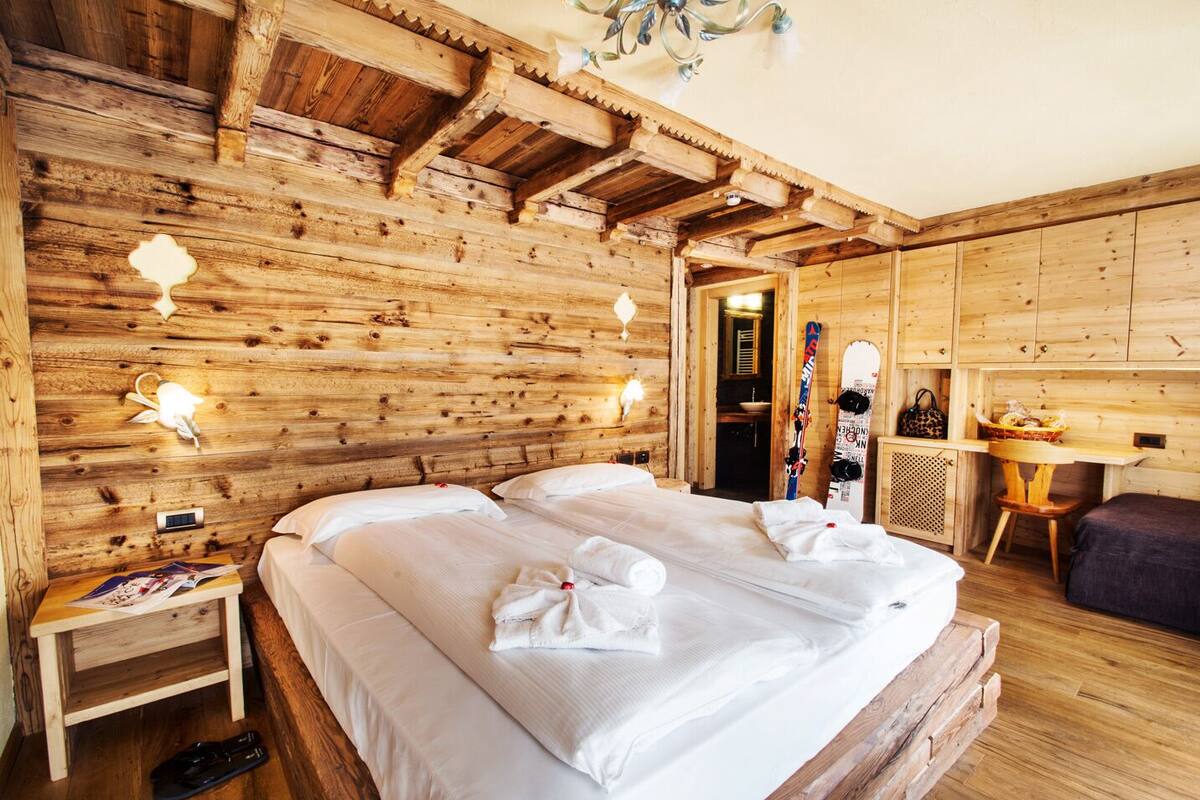 A wooden cabin room with a bed, bedside table, and skis leaning against the wall.