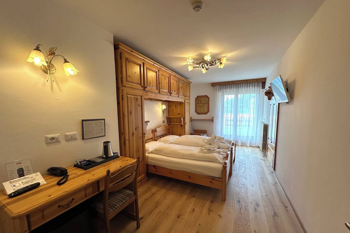 A room with a wooden desk, a bed, and a chandelier.
