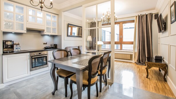 A modern kitchen with white cabinetry, a built-in oven, and a dining area with a table and chairs. - Exclusive Apartments Warsaw City Centre (Warsaw)