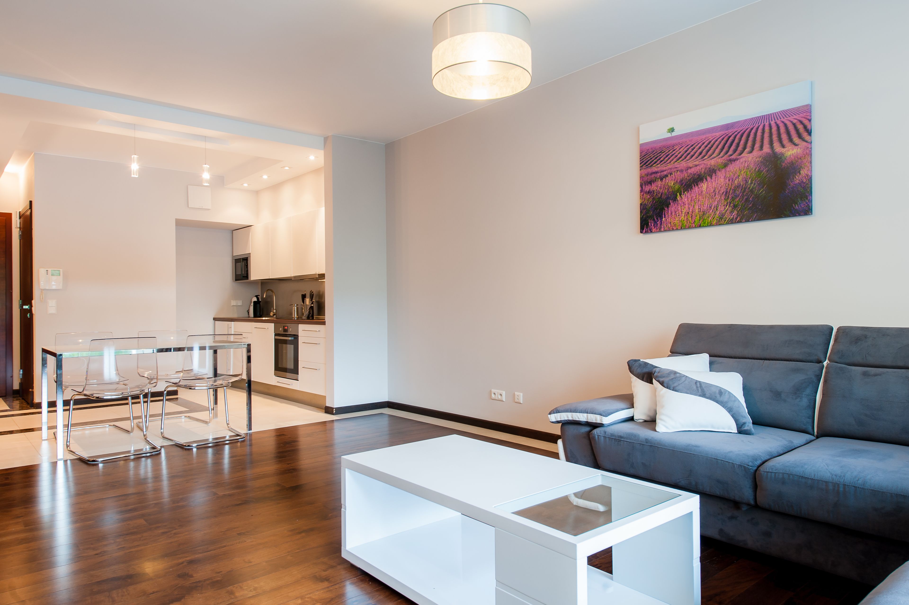 Una sala moderna con un sofá gris, una mesa de centro de vidrio y un comedor con mesa y sillas de vidrio.
