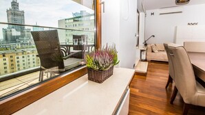 A modern living room with a large window, a wicker chair, a sofa, and a small table with a plant. - Exclusive Apartments Warsaw City Centre (Warsaw)