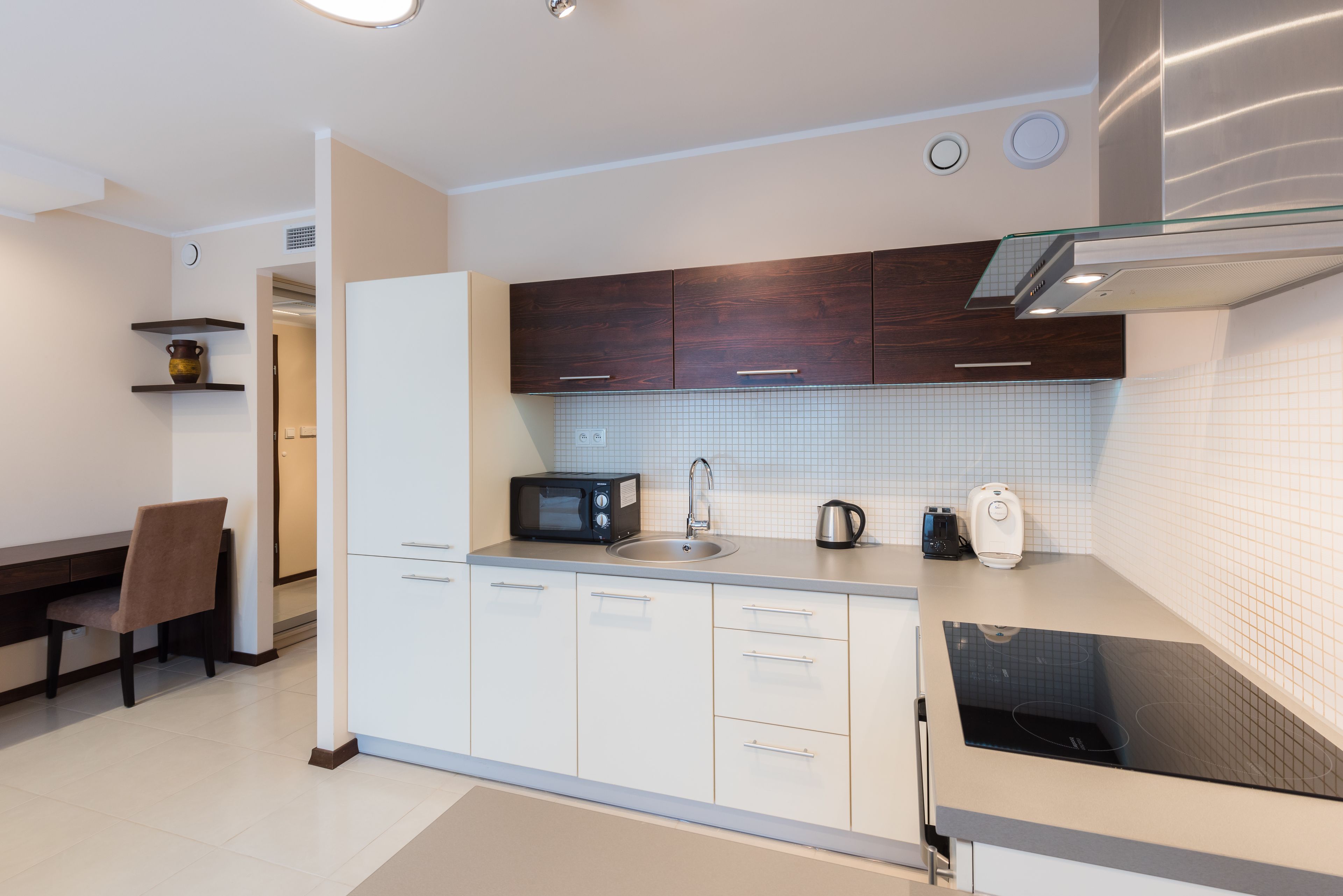 A modern kitchen with white cabinets, a microwave, a kettle, and a built-in stove.