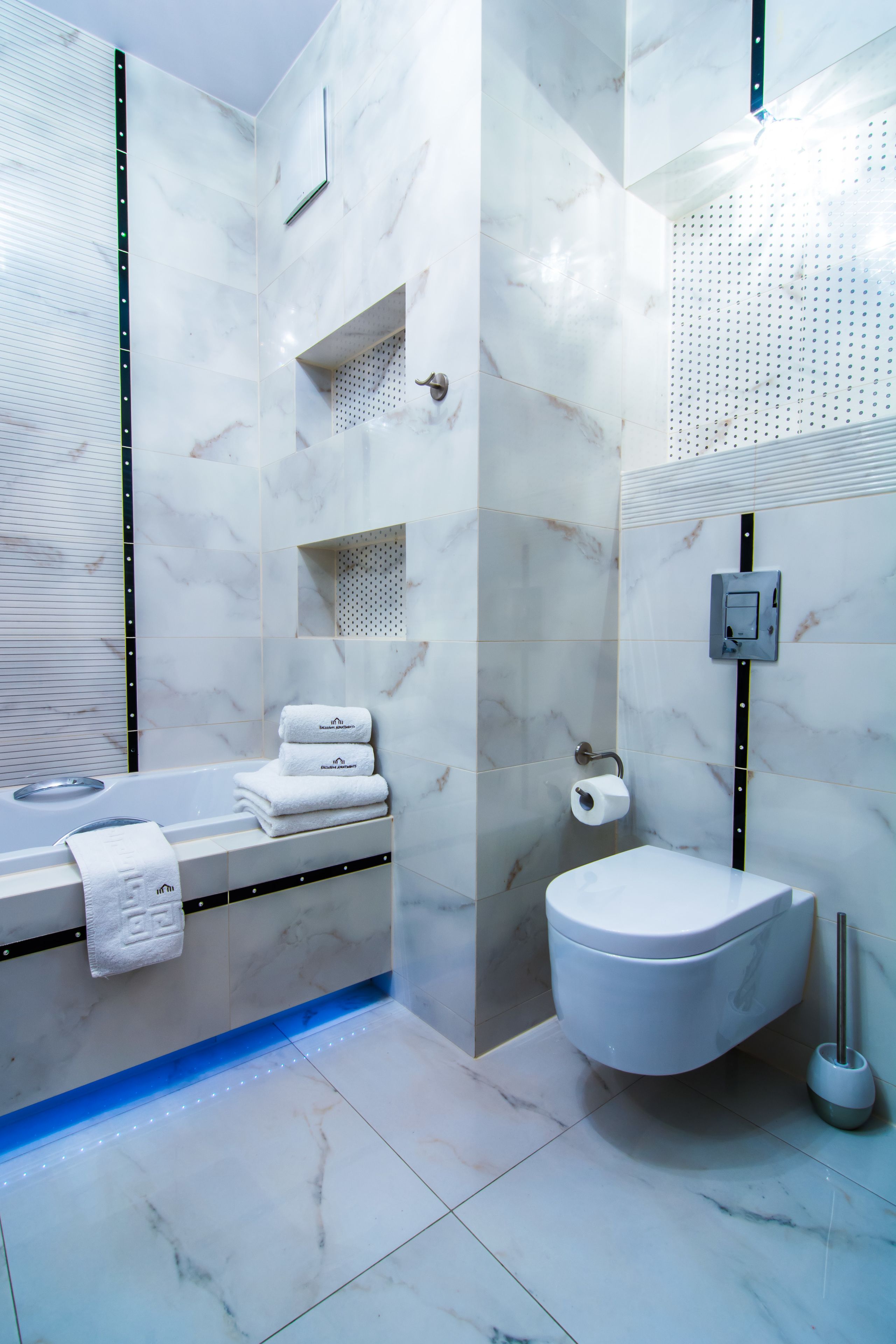 A modern bathroom with a marble floor, a bathtub, a toilet, and a shower area.
