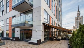A modern hotel with a glass facade, outdoor seating, and a view of a historic building in the background. - Exclusive Apartments Warsaw City Centre (Warsaw)