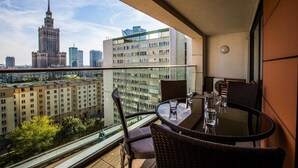Ein Balkon mit Tisch und Stühlen, der auf einen Stadtblick mit modernen Gebäuden und einem historischen Turm zeigt.
