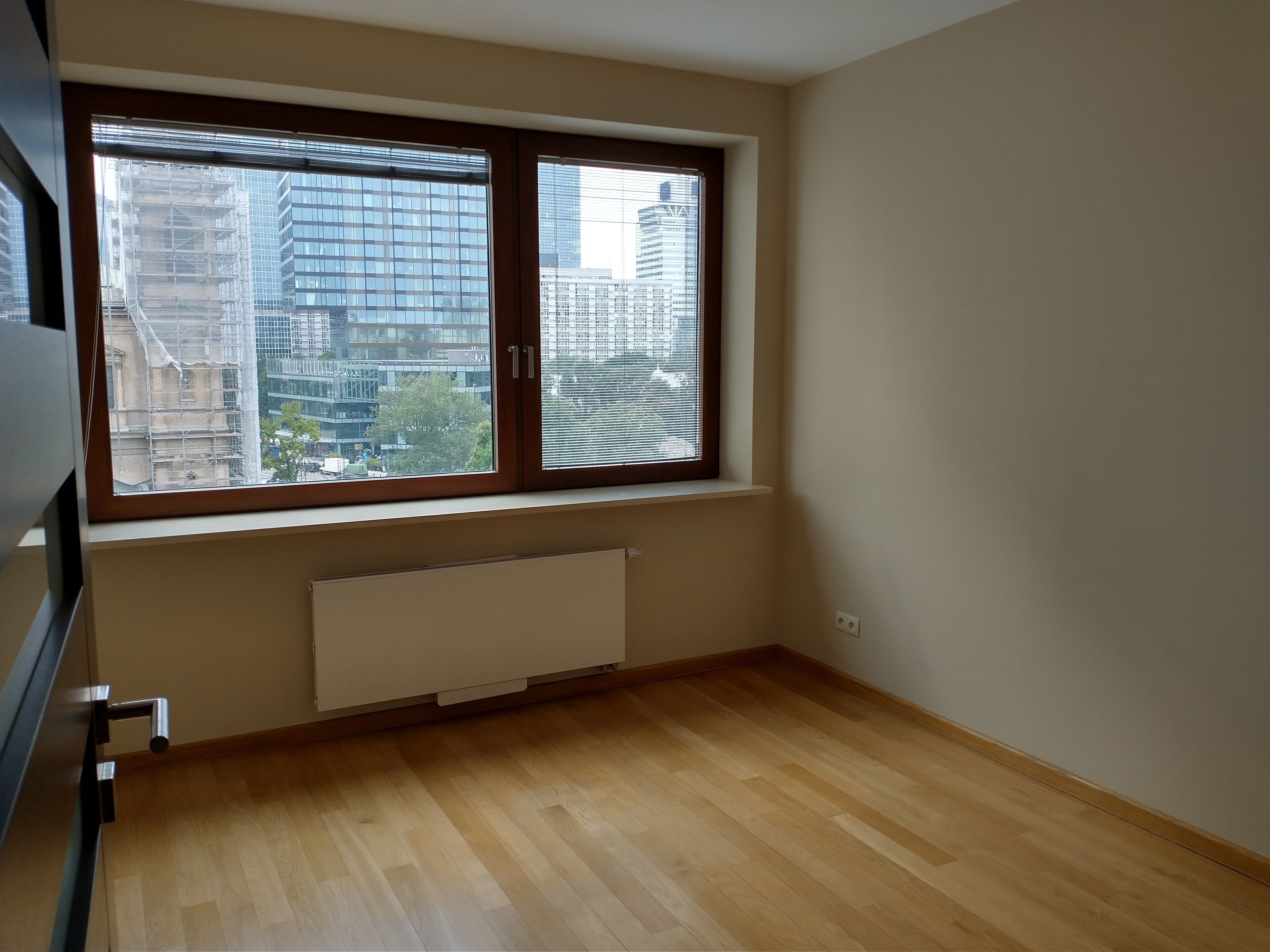 A room with a large window, wooden flooring, and a white radiator.