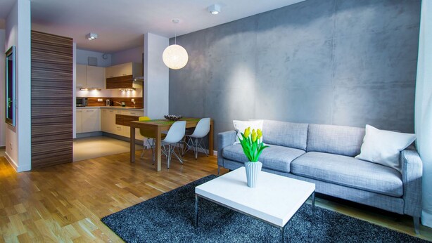 Ein modernes Wohnzimmer mit einem grauen Sofa, einem weißen Couchtisch und einem Essbereich mit einem Holztisch und Stühlen.
