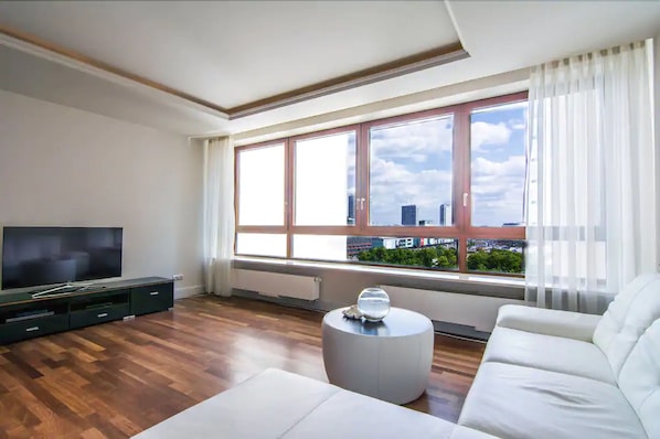 A modern living room with a flat-screen TV, a white sofa, a round coffee table, and a large window with a city view. - Exclusive Apartments Warsaw City Centre (Warsaw)